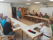 Die beiden Simultanspieler stehen in der Mitte eines Raumes, rundherum die Simultangegner vor ihren Schachbrettern