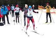 Das Bild zeigt eine lebhafte Szene eines Langlauf-Events auf einem schneebedeckten Kurs. Im Zentrum des Geschehens befindet sich eine aktive Langläuferin (Erna Berger) mit der Startnummer 25, die dynamisch auf ihren Skiern fährt und ihre Skistöcke nu